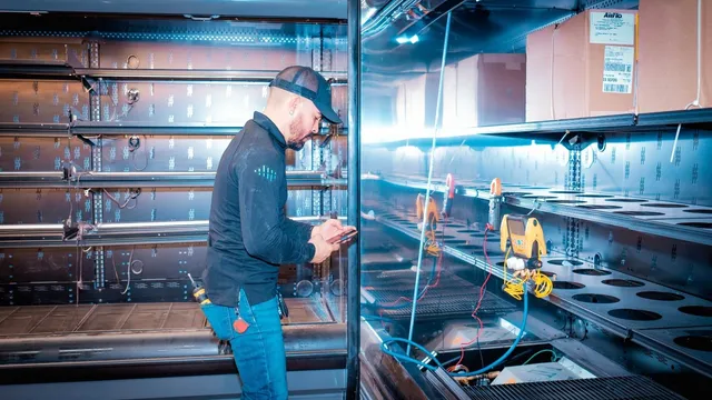 A Dynamiq technician taking readings on an emptied Key Food display case, with clamp meters and gauges wired to the unit while it is out of service